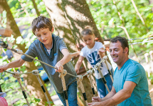 Kind klettert im Waldseilgarten Erwachsener hilft